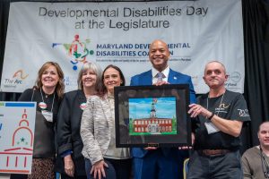 Joe Harter presents Governor Wes Moore with artwork of the Maryland State House. They are joined on stage by Ande Kolp, Laura Howell, and Rachel London. Photo by Jennifer Bishop.