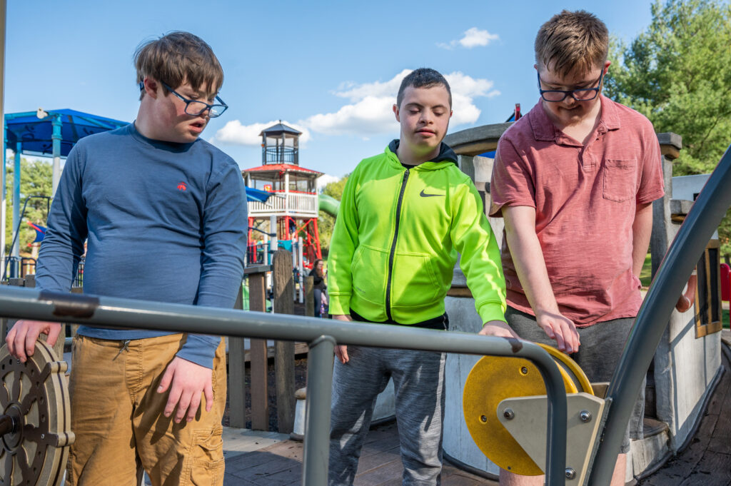 Three teenage boys with developmental disabilities play together on a playground. 