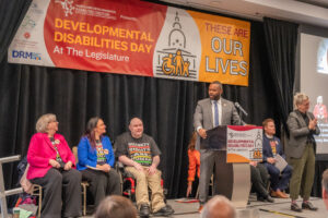 Senator Cory McCray speaks on stage during DD Day. DD Coalition leaders are sitting behind him.