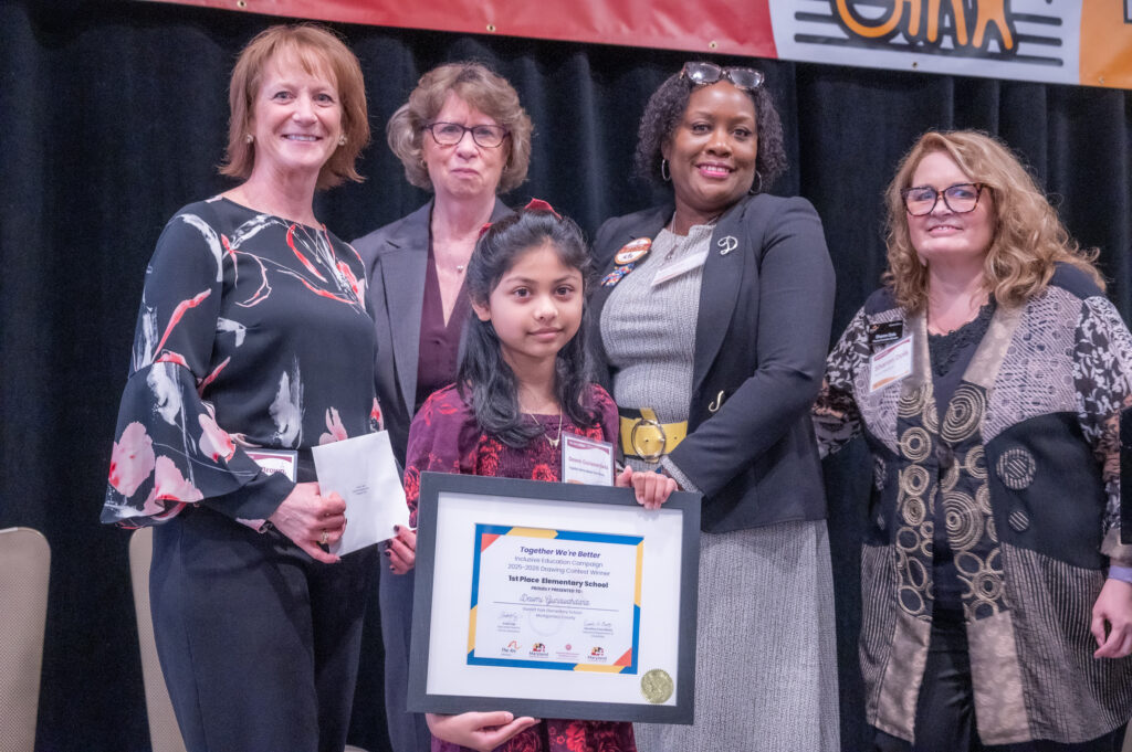 A young girl stands on stage after winning an award for the Together We're Better artwork contest. She is joined on stage by representatives from MSDE, MDOD, the DD Council, and The Arc Maryland.